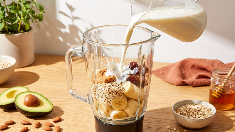 Milch wird in einen Mixer mit Banane, Haferflocken, Erdnussbutter und Datteln gegossen – Tipps zum gesunden Zunehmen