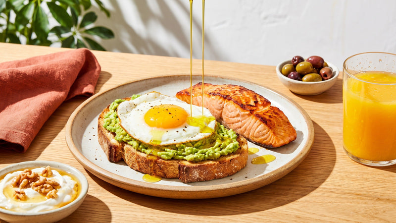 Kalorienreiche Mahlzeit mit Avocado-Toast, Spiegelei, Lachs, Olivenöl, Joghurt mit Walnüssen und Orangensaft – Tipps zum gesunden Zunehmen