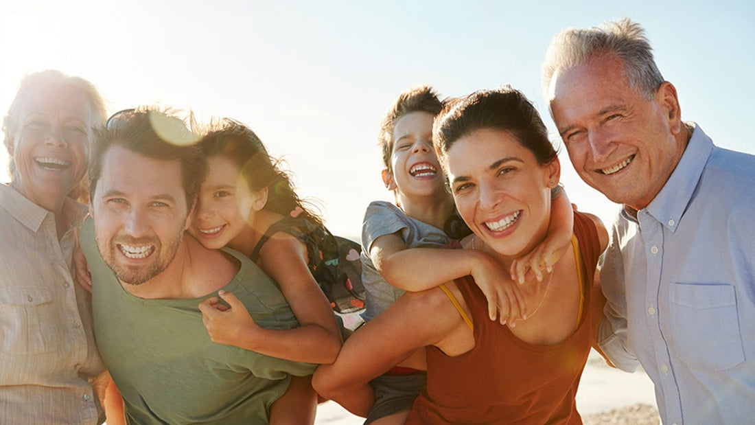 Drei Generationen einer Familie lachen gemeinsam am Strand im Sonnenlicht – CaloShop Community